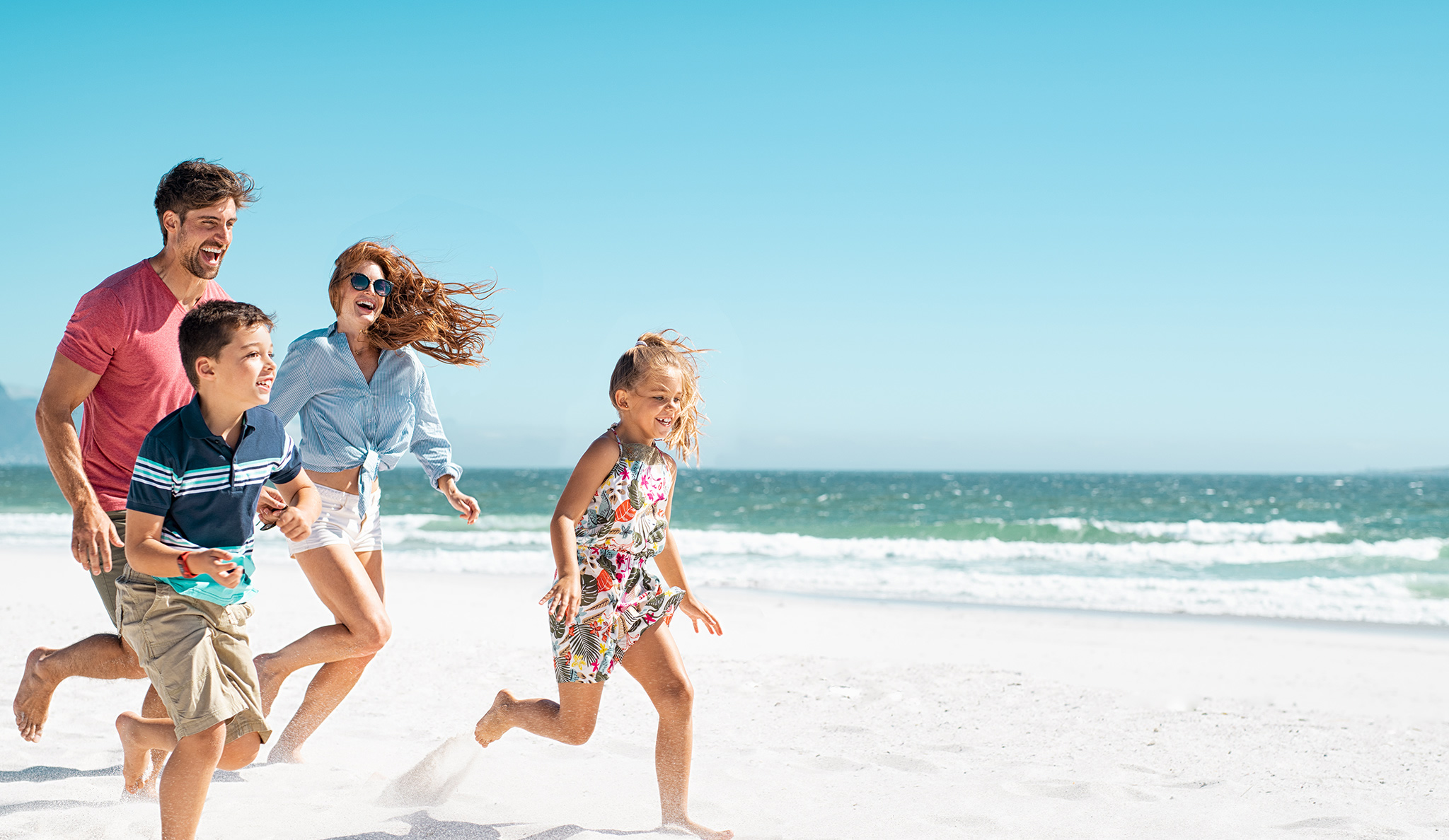family with parents and kids happily running on a beautiful beach